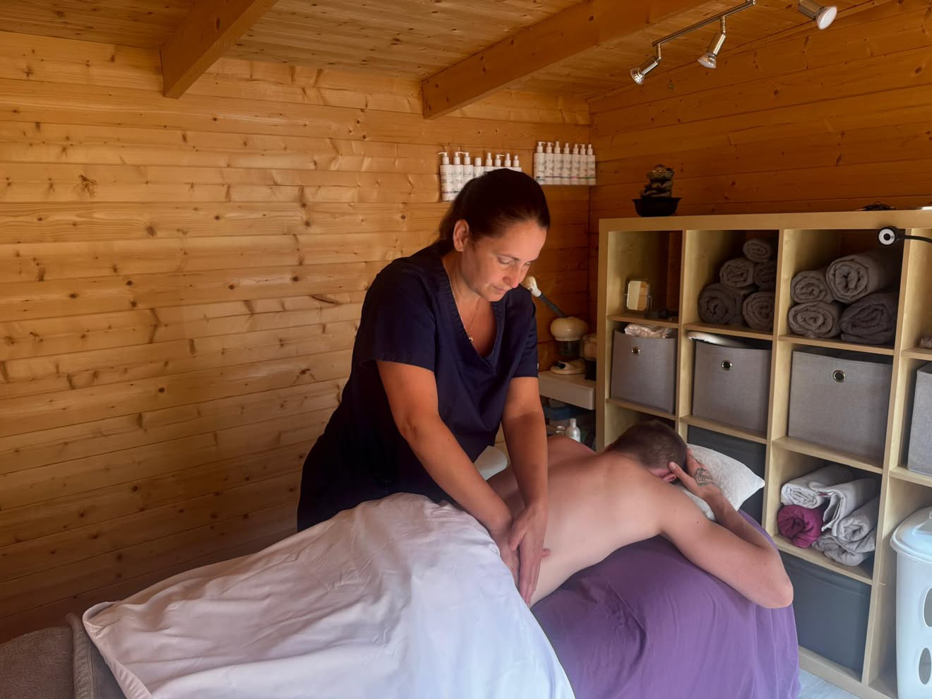 Diane working on a client's lower back, with cabin shelves in the background